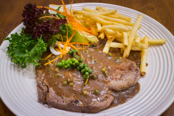 Healthy Beef steak with black pepper sauce & salad in a white dish on wood table background for ready to serve.