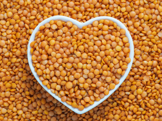 Red orange lentil Football in heart bowl on lentils background