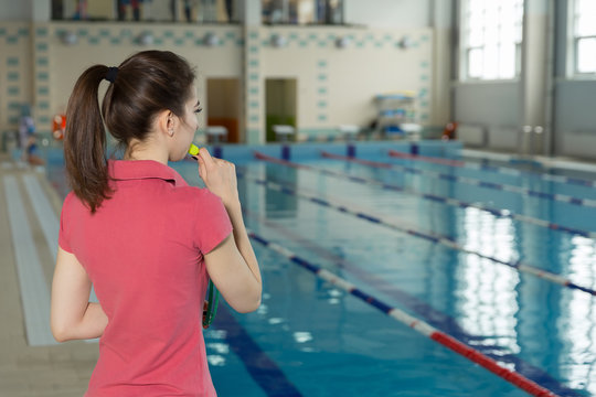 trainer woman blowing whistle and standing with his back near poolside