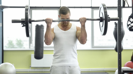 Naklejka premium athlete doing exercise for biceps with barbell. young muscular man trains at the gym