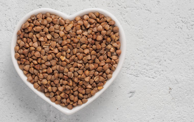 Heart-shaped bowl of roasted buckwheat on gray cement background