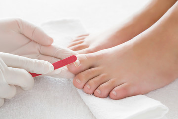 Hands in gloves cares about a woman's foot nails. Pedicure, manicure beauty salon concept. Fingernails filing with file.