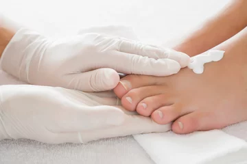 Fotobehang Hands in gloves cares about a woman's foot. Pedicure beauty salon concept. Foot moisturizing cream. © fotoduets