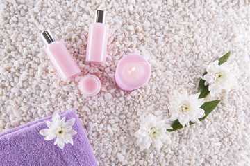 Spa. Still life. Candle, bottles with cream of pink color, a towel and flowers on a background of white pebbles. Top view
