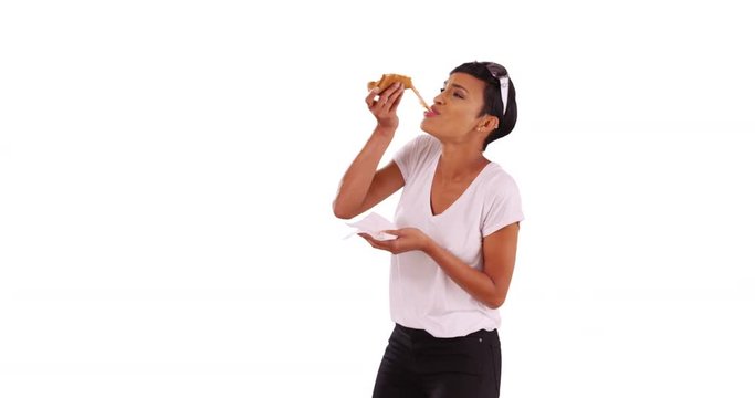 Stylish black female eating a slice of delicious cheese pizza on white background with copyspace. Young woman in her 20s enjoying lunch, smiling and laughing in studio 