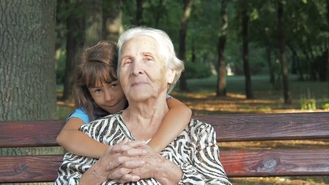 Children are hugging an elderly grandmother. Happy little granddaughter with grandmother in the park.