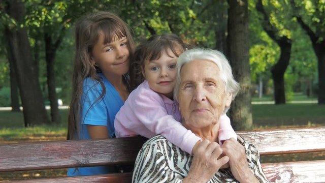 Children are hugging an elderly grandmother. Happy little granddaughter with grandmother in the park.