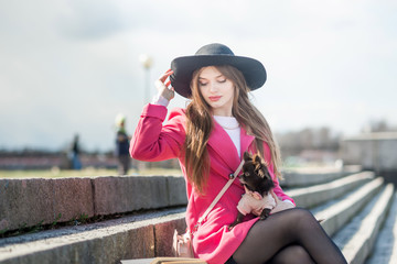 girl in a pink coat and a black hat with a small dog