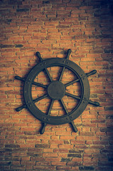 Steering wheel for ship showing on red brick wall background.