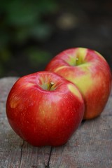 Two ripe red apples on a wooden surface.