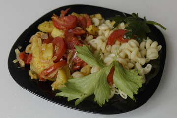 Pasta with stewed vegetables on a black dish isolated on a white background
