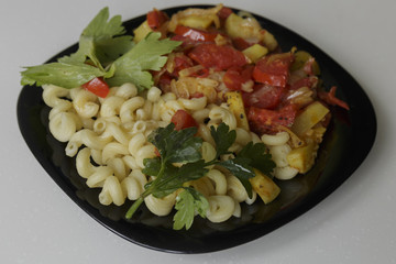 Pasta with stewed vegetables on a black dish isolated on a white background