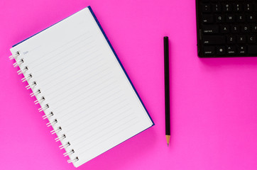 White note book and black pencil and black keyboard on pink color background with copy space.