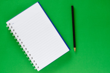 White note book and black pencil on green color background with copy space.