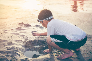 Asian child has fun digging in the sand. Young boy enjoying on beach.