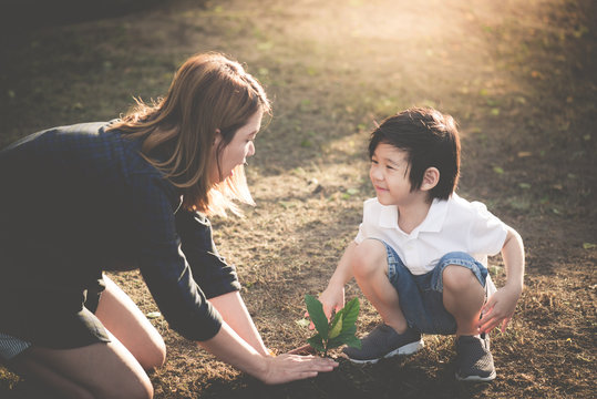 Cute Asian child and mother planting young tree on the black soil