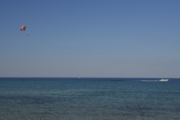 Parasailer and a boat against blue sky and sea.