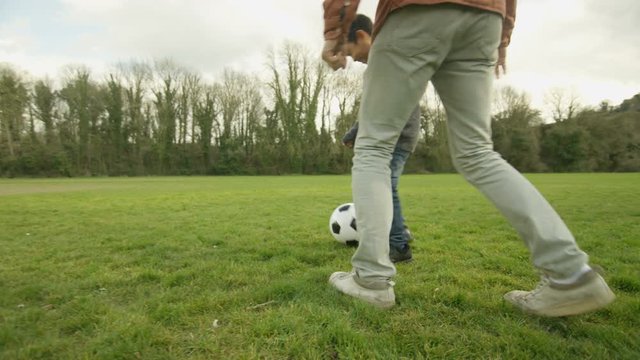  Happy young Asian father & son playing football outdoors & having fun