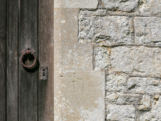 Old weathered wooden door with rusty iron lock and knocker on ancient stone wall