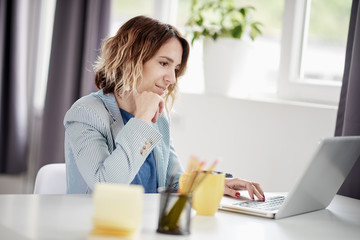 Businesswoman using laptop and drinking coffee while sitting at modern home office