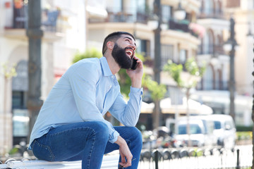 Side of laughing man sitting outside talking on mobile phone