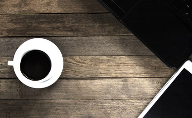 White coffee cup and black notebook on rustic wooden table. Black screen smartphone on empty table.