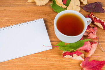 blank notepad with autumn leaves and tea cup on rustic table