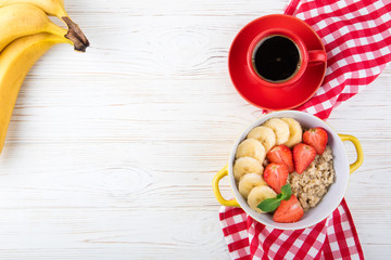 Breakfast with oatmeal porridge, coffee cup, berries and fruits. Oatmeal with strawberries and banana. Healthy breakfast concept. Top view