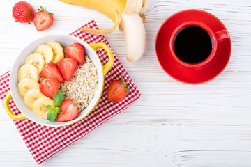 Breakfast with oatmeal porridge with fruits and berries. Coffee cup. Oatmeal with strawberries and banana. Healthy breakfast concept. Top view