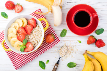 Breakfast with oatmeal porridge with fruits and berries. Coffee cup. Oatmeal with strawberries and banana. Healthy breakfast concept. Top view