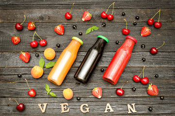Fototapeta na wymiar Three bottles with juice, fruit and inscription vegan on a dark wooden background, food concept