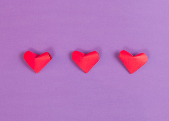 Three Red Paper Origami Hearts on Purple Background
