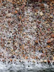 Water falling from top on stone wall in a park for use as background