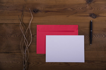 Top view of envelope and blank greeting card with flowers on  wooden background. Desktop with blank page mock up, open envelope. Creative concept, empty greeting card