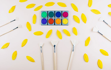 Watercolor and brushes at beige background.