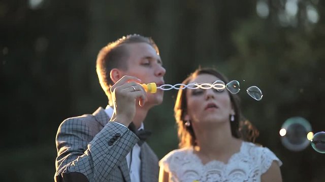 beautiful bride and groom laugh and blow soap bubbles in the park at sunset