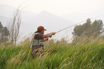 Portrait of fly-fisherman at sunset in country field
