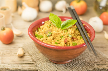 Bulgur or pilaf or risotto or East barley porridge with mushrooms and vegetables and basil in ceramic pottery bowl with chopsticks rustic style on rural wooden table