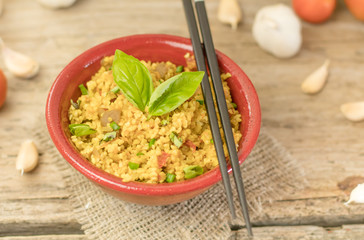 Bulgur or pilaf or risotto or East barley porridge with mushrooms and vegetables and basil in ceramic pottery bowl with chopsticks rustic style on rural wooden table