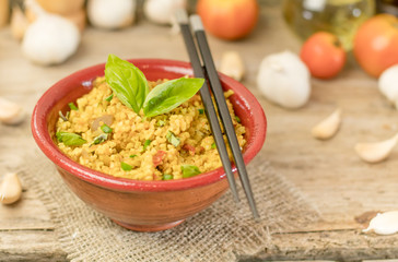 Bulgur or pilaf or risotto or East barley porridge with mushrooms and vegetables and basil in ceramic pottery bowl with chopsticks rustic style on rural wooden table