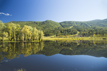 Autumn colors of a mountain lake and forests on the banks. Clear reflection of trees on a smooth water surface. A clear, sunny day.