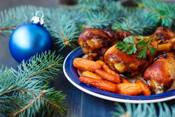 Chicken legs baked in honey and soy sauce with baked carrots Christmas recipe, decorated with fir branches.