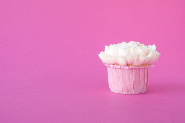 Pink cupcake with white whipped cream in form of flower on pink background. Picture for a menu or a confectionery catalog.
