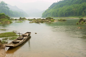 Fototapeta na wymiar Traditional wooden boat tied at a river bank in rainy weather in Chengyang, Guangxi, China.