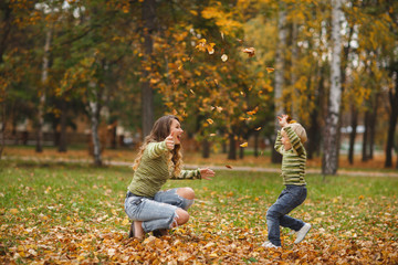 Fototapeta premium Young beautiful mother with her children on the autumn background. Pretty mom and her little sons having fun together outdoors in fall time. Cheerful family