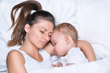 Fototapeta na wymiar young beautiful mother sleeps and hugs with her little cute son on white linen 