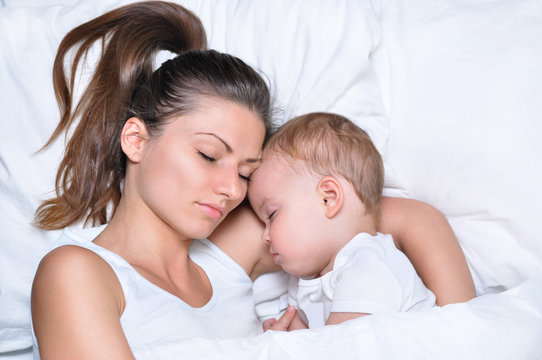 young beautiful mother sleeps and hugs with her little cute son on white linen
