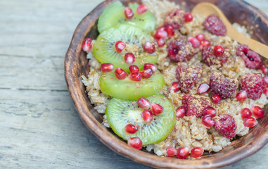 Healthy diet wellness cereal flakes homemade breakfast: Glass or ceramic Bowl of oatmeal wheat rye porridge, hot healthy food with fruits and berries: kiwi, peeled pomegranate seeds, raspberries