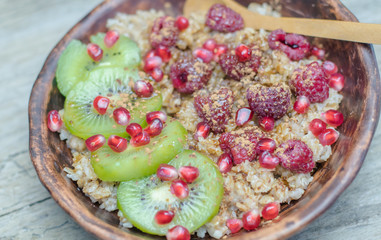 Healthy diet wellness cereal flakes homemade breakfast: Glass or ceramic Bowl of oatmeal wheat rye porridge, hot healthy food with fruits and berries: kiwi, peeled pomegranate seeds, raspberries