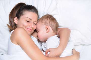 Fototapeta na wymiar young beautiful mother hugs with her sleeping little cute son on white linen 